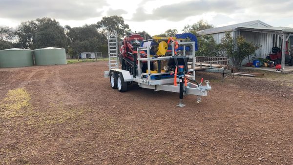 Galvanised tandem plant trailer loaded with the red mini loader, trencher, auger and attachments