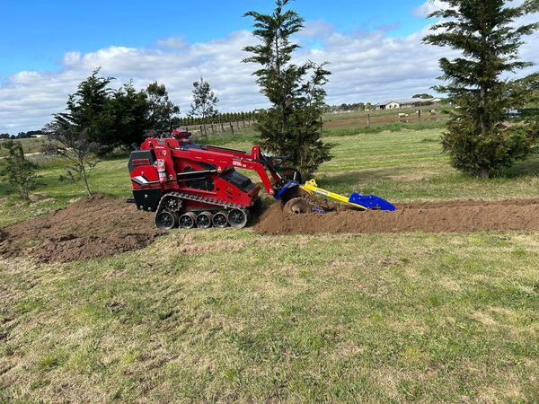 Red Darlington tracked mini loader trenching across a green lawn with trees