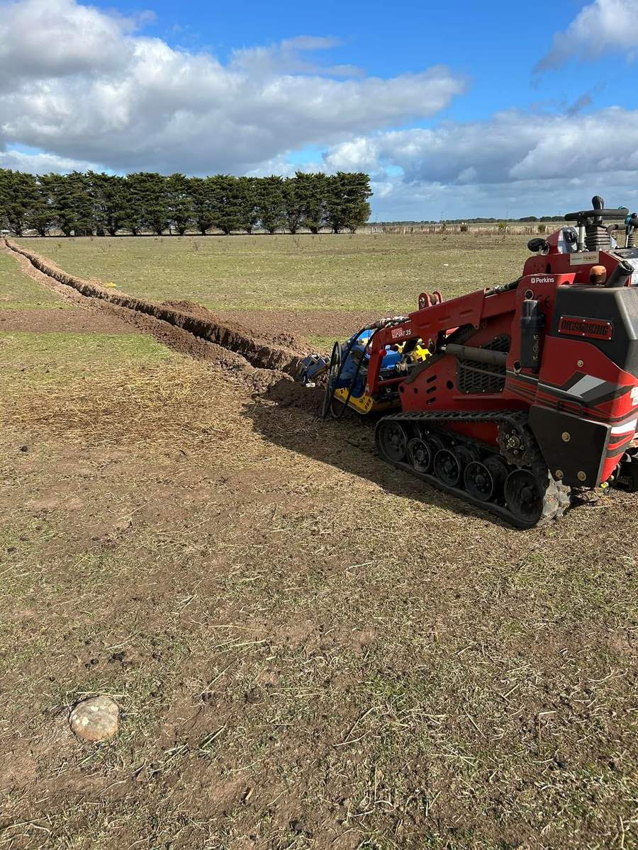 Red Darlington tracked mini loader with a trencher attachment digging a long trench across a paddock